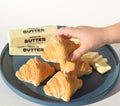 Hand picking a croissant candle from a plate with other croissant candles and blocks of butter.