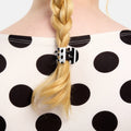 Person with a braid wearing a black hair clip on a polka dot background