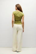 A woman shown from the back wearing a sage green short-sleeve top and cream wide-leg trousers, standing against a plain white studio background.