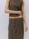Person wearing a brown plaid top and skirt on a light gray background