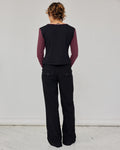 A model viewed from the back wearing a sleeveless black vest over a long-sleeve top with red and white stripes, paired with black pinstriped trousers, against a plain light gray wall.